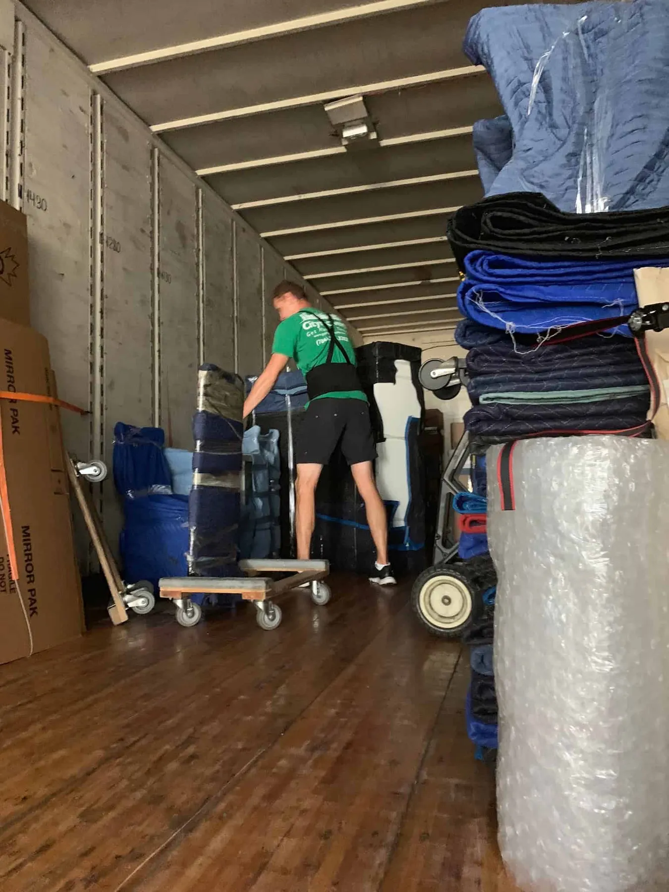 Crew member loading furniture wrapped in moving blankets inside a truck