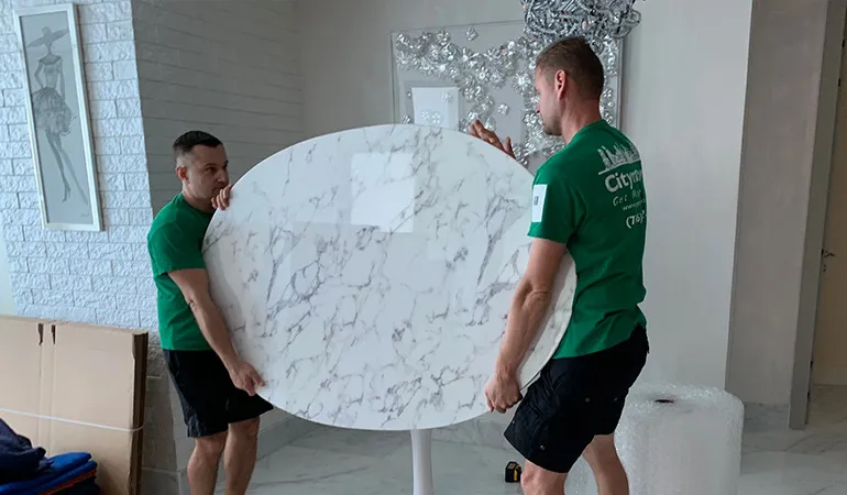Two movers carrying a marble table top through a condo