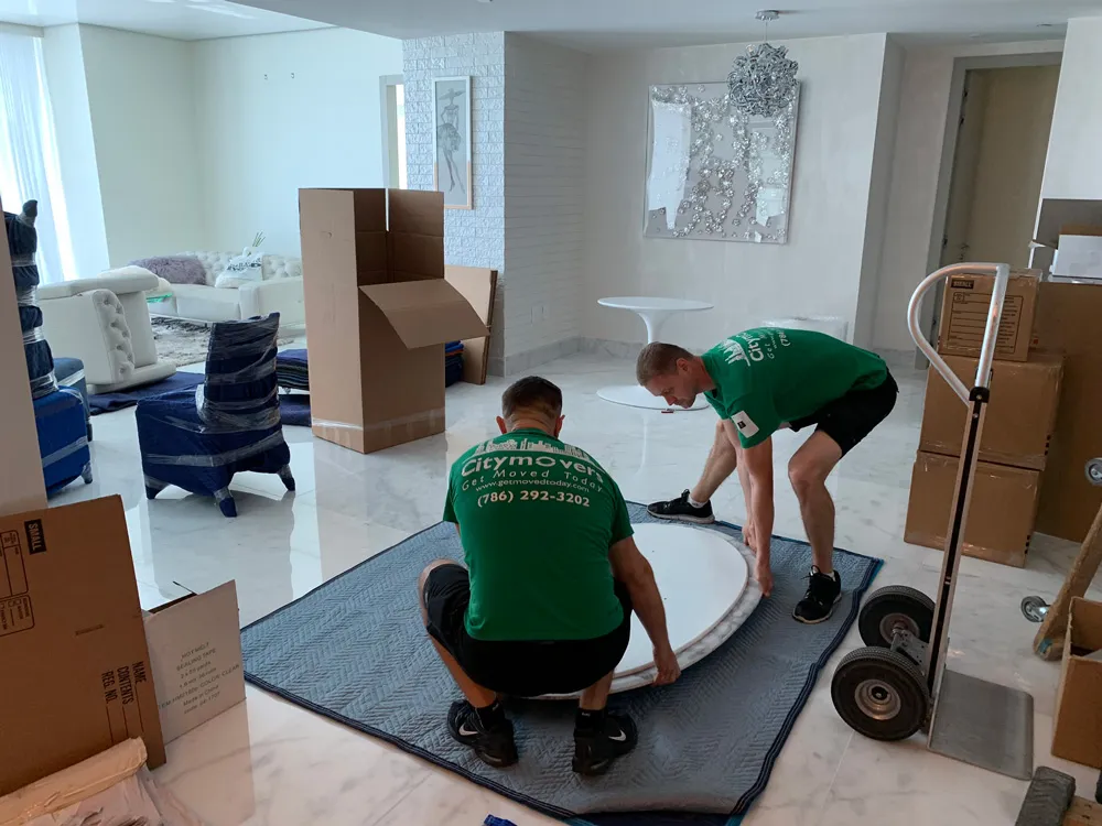 Two movers preparing furniture with a hand truck and moving pads